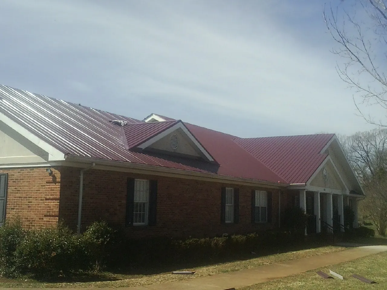 Red metal roof with gabled entries on a long brick building, from a Hail Damage Roof Repair job in Shamokin