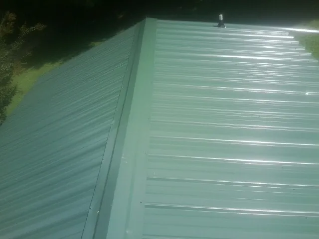 New green metal panels meeting at the ridge of a roof — Flat Roof Repair work by our crew in Shamokin