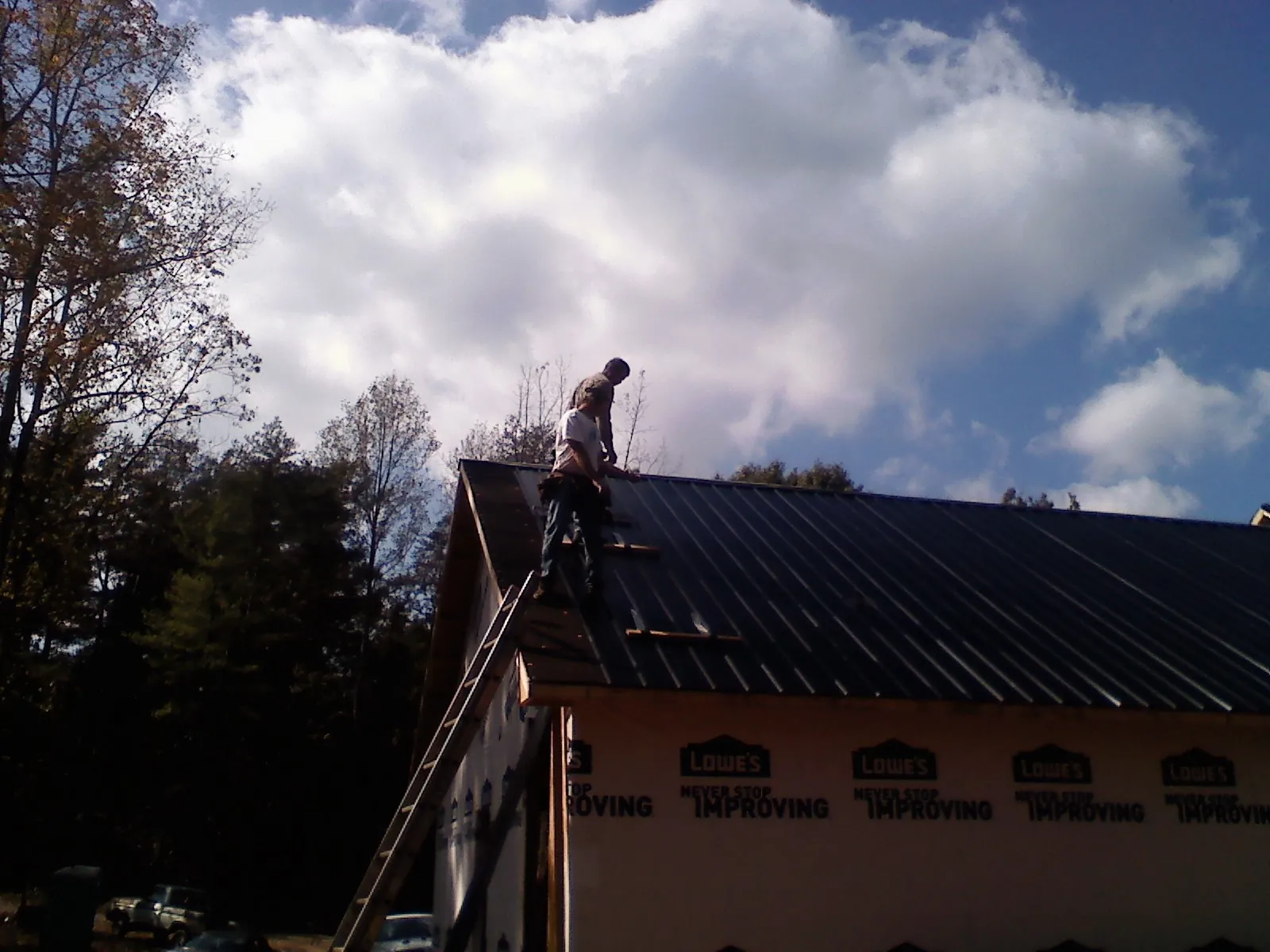 Roofer fastening dark metal panels high against a cloudy sky, from a Roof Inspection job in Shamokin