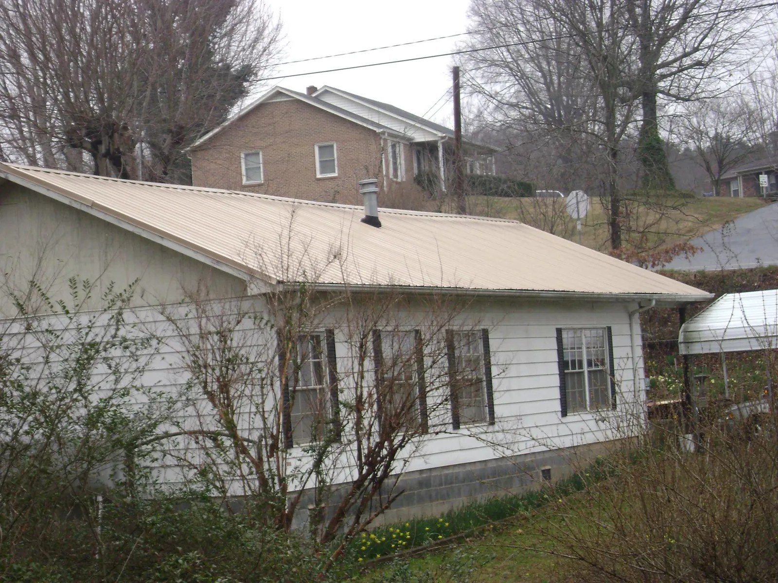 Tan metal roof on a white sided house set into a hillside — Commercial Roofing by Roofing Brothers in Shamokin